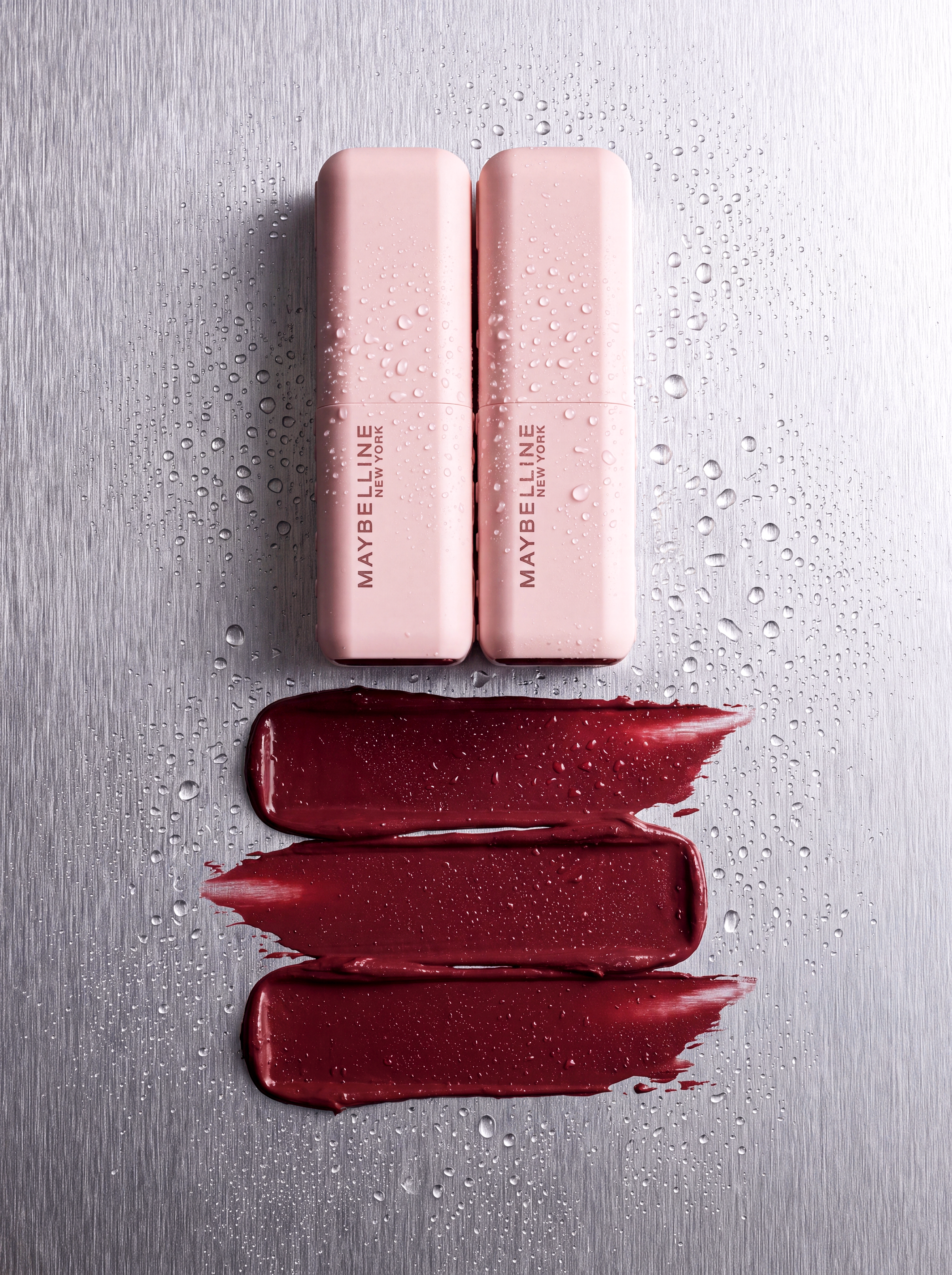 Top view product composition with pale pink cosmetic objects, red texture, and water drops on metal